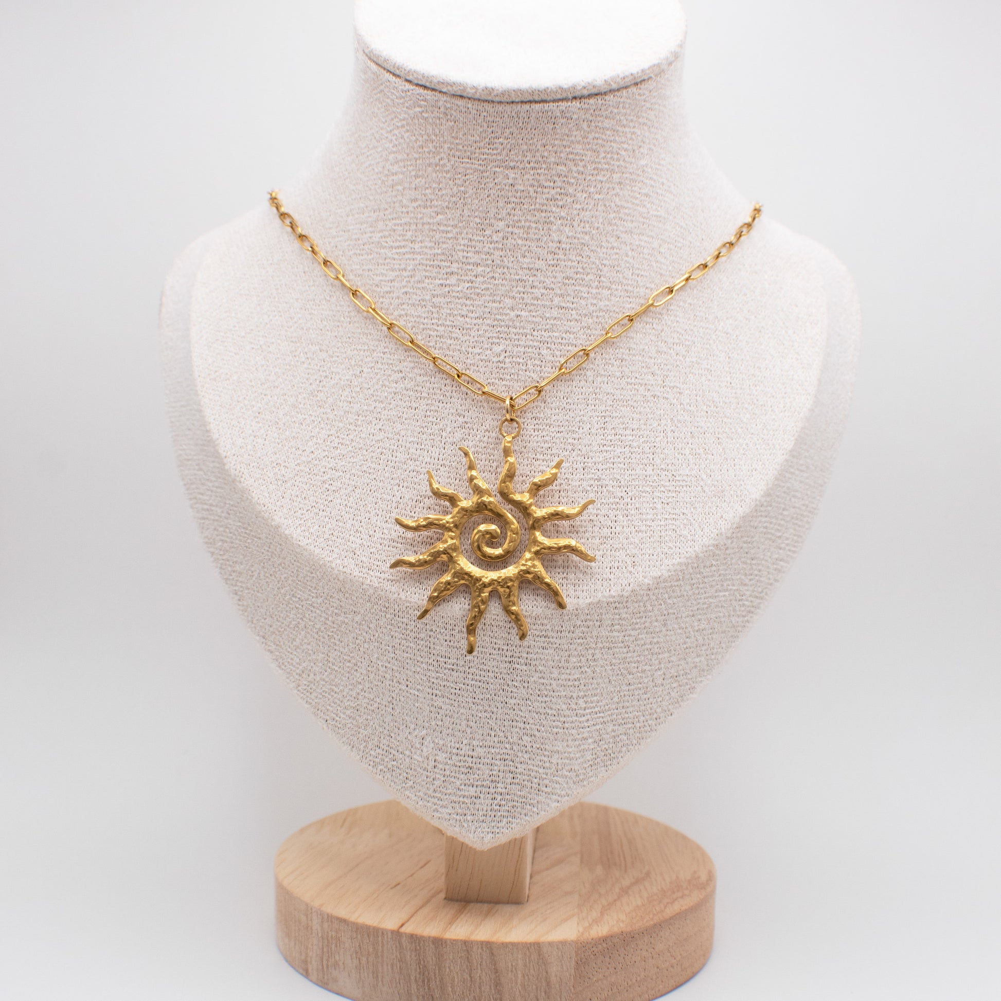 Gold sun-shaped pendant necklace on a mannequin bust with a white background