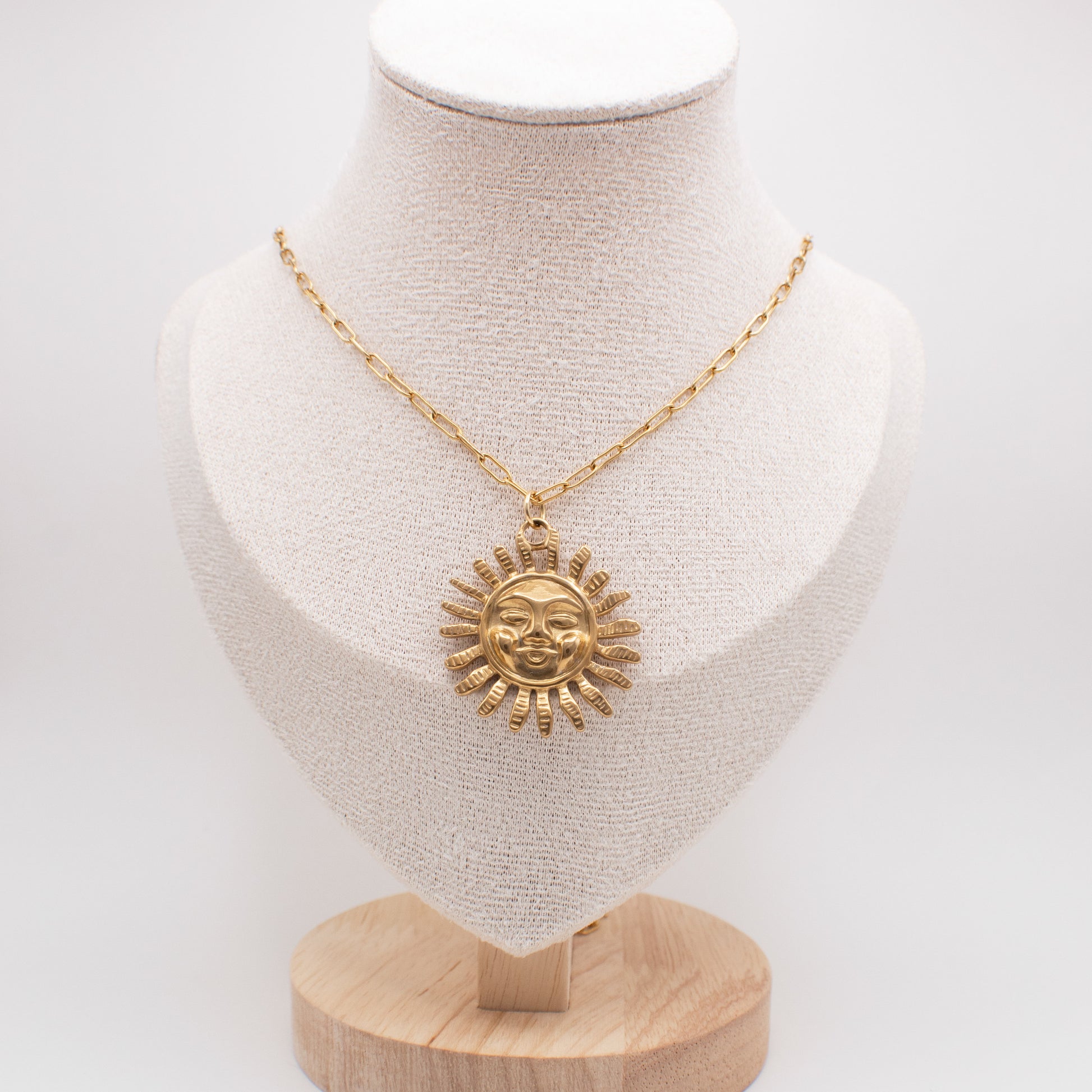 Gold necklace with sun pendant on a mannequin bust against a white background