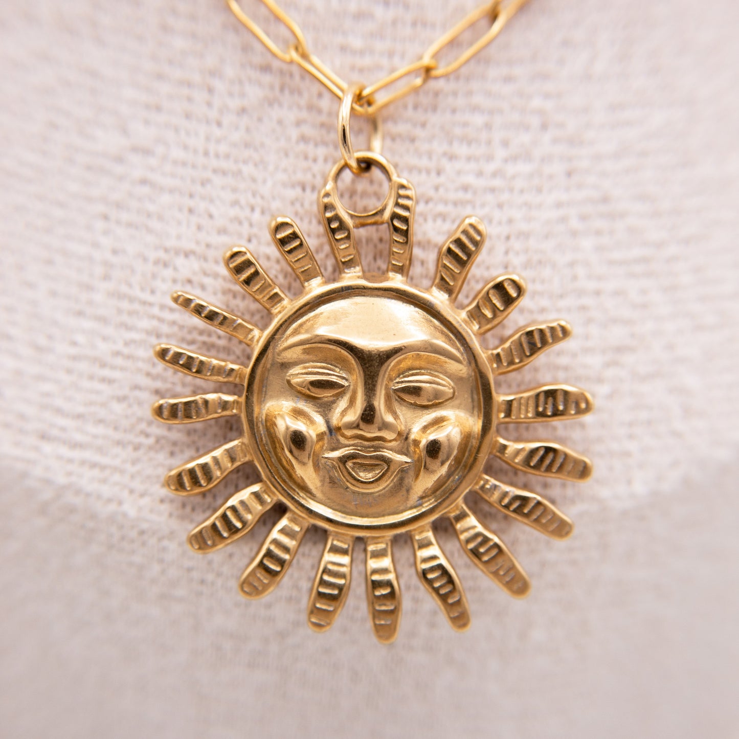 Gold sun-shaped pendant with face design on a light beige background