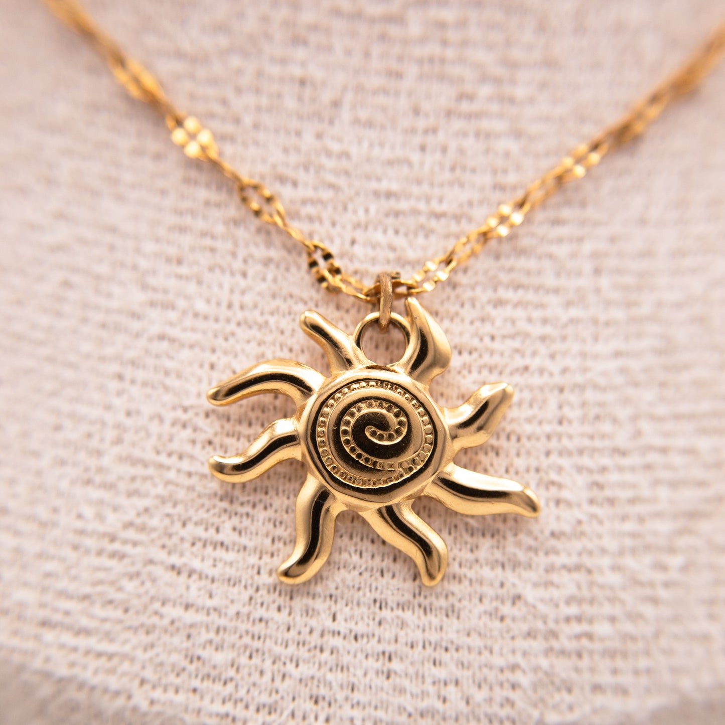 Gold sun-shaped pendant necklace on a beige fabric background