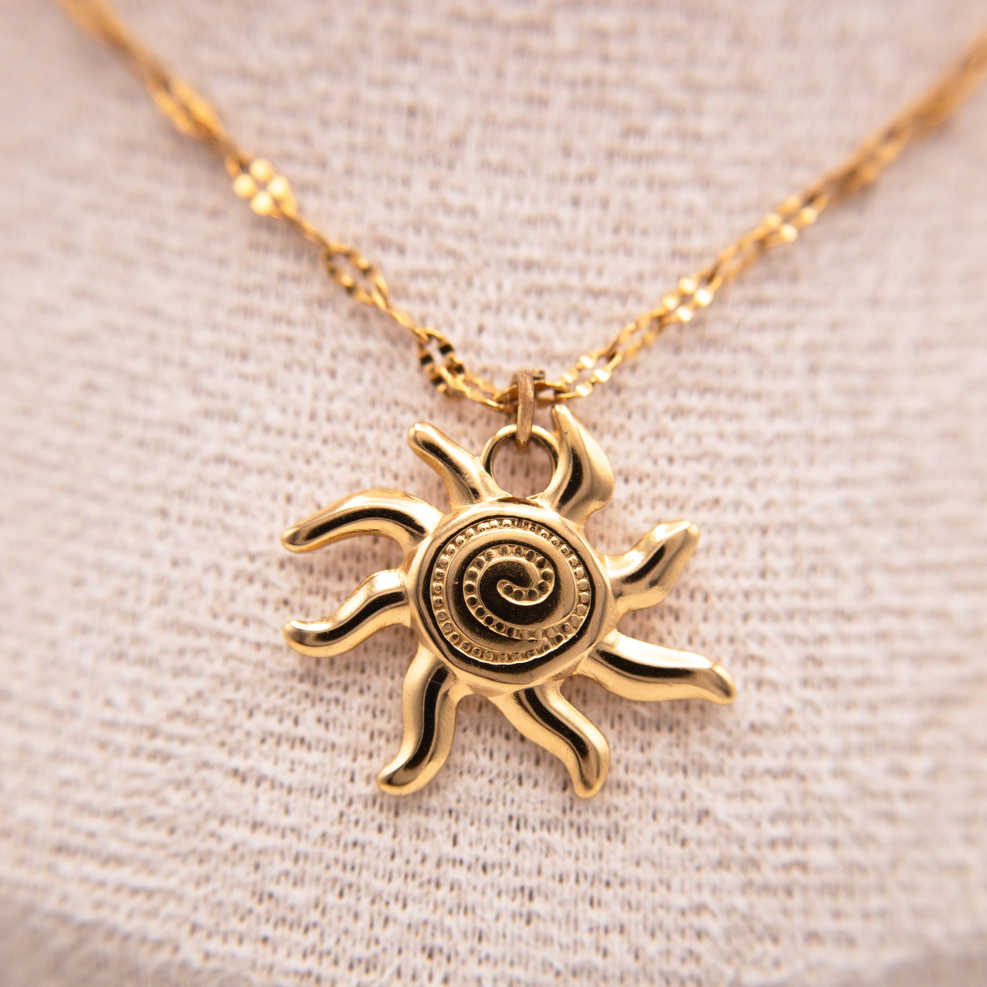 Gold sun-shaped pendant necklace on a beige fabric background