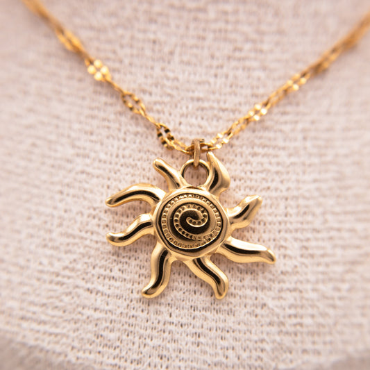 Gold sun-shaped pendant necklace on a beige fabric background