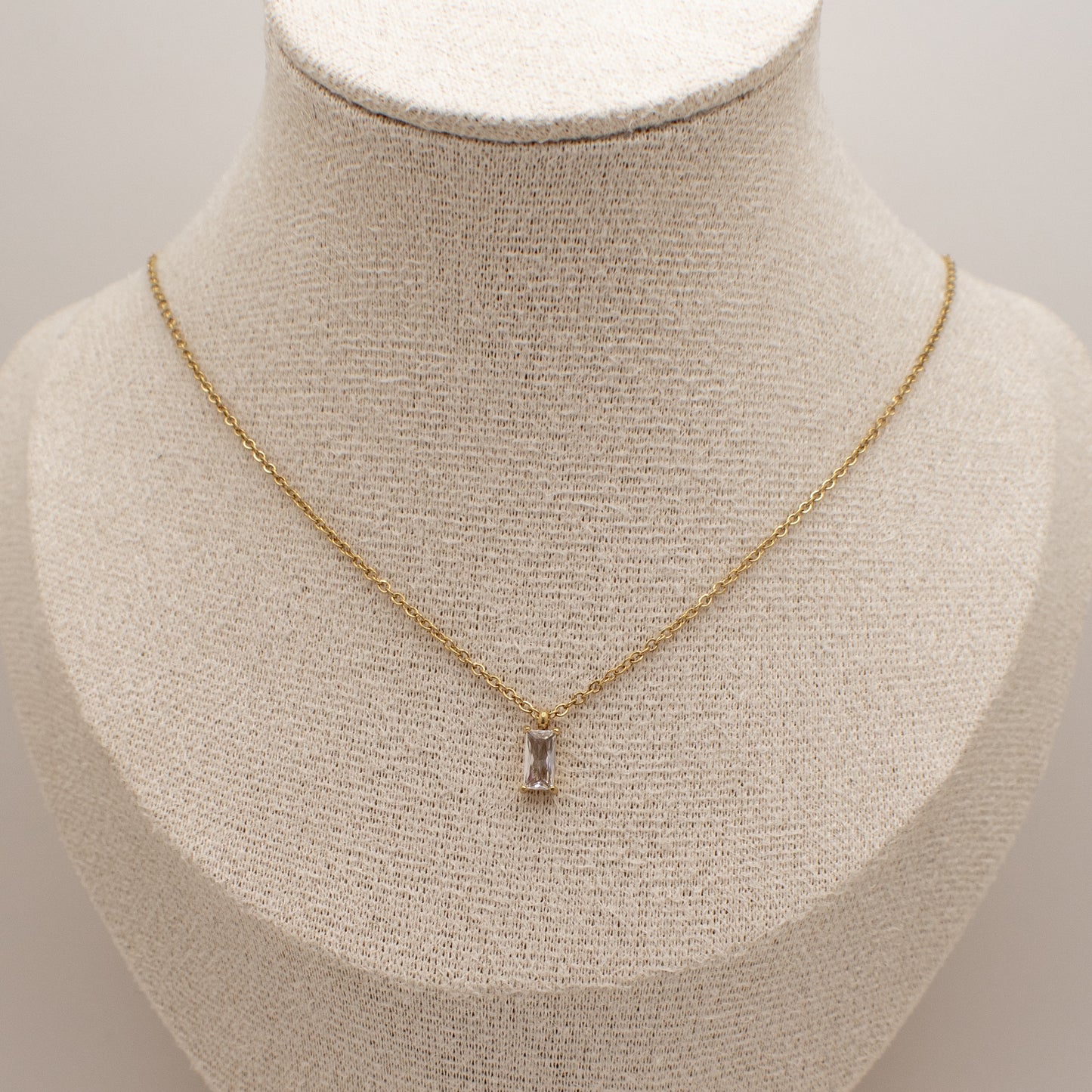 Gold necklace with a pendant on a mannequin bust against a neutral background