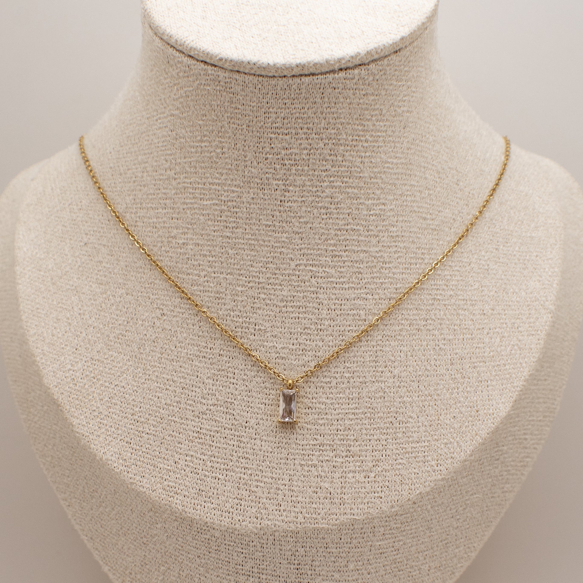 Gold necklace with a pendant on a mannequin bust against a neutral background