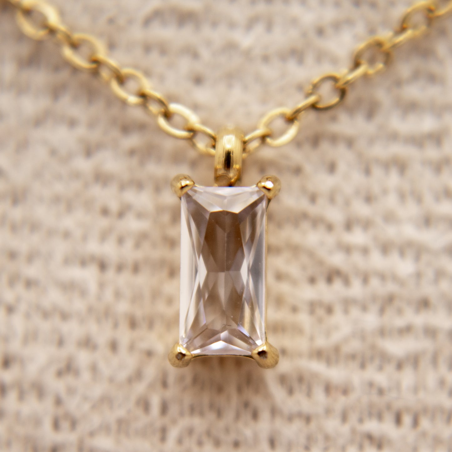 Gold necklace with a rectangular gemstone pendant on a beige fabric background