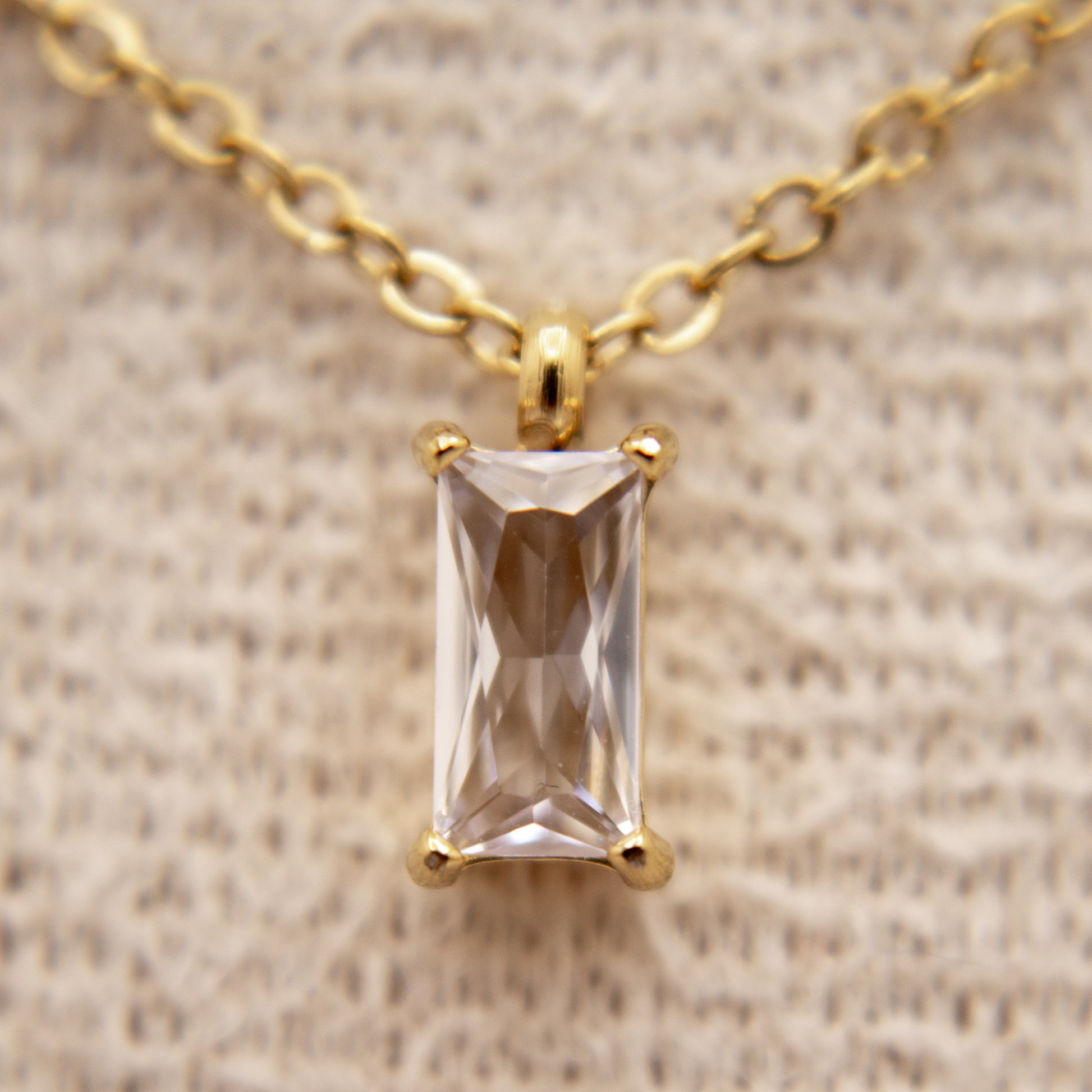 Gold necklace with a rectangular gemstone pendant on a beige fabric background