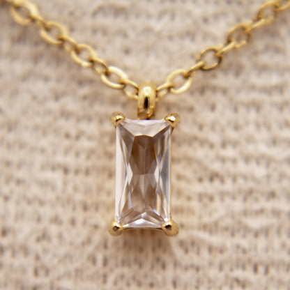 Gold necklace with a rectangular gemstone pendant on a beige fabric background