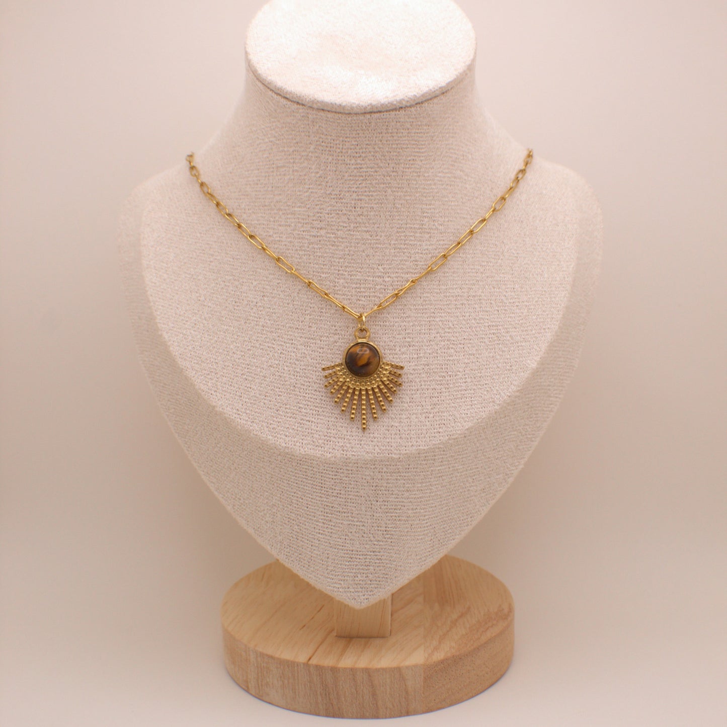 Gold necklace with a pendant on a mannequin bust against a plain background