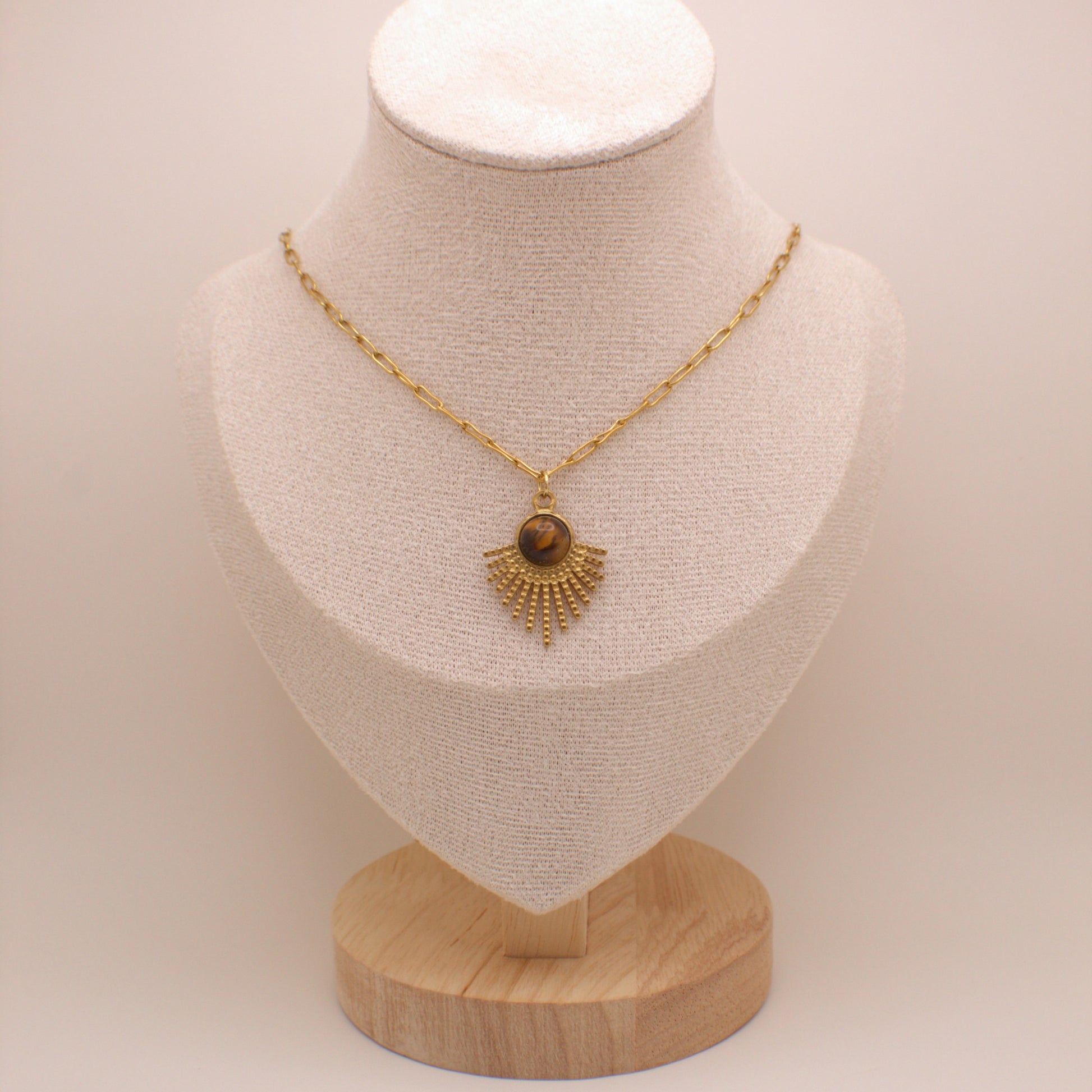 Gold necklace with a pendant on a mannequin bust against a plain background