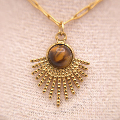 Gold necklace with a sunburst pendant featuring a tiger's eye stone on a beige fabric background