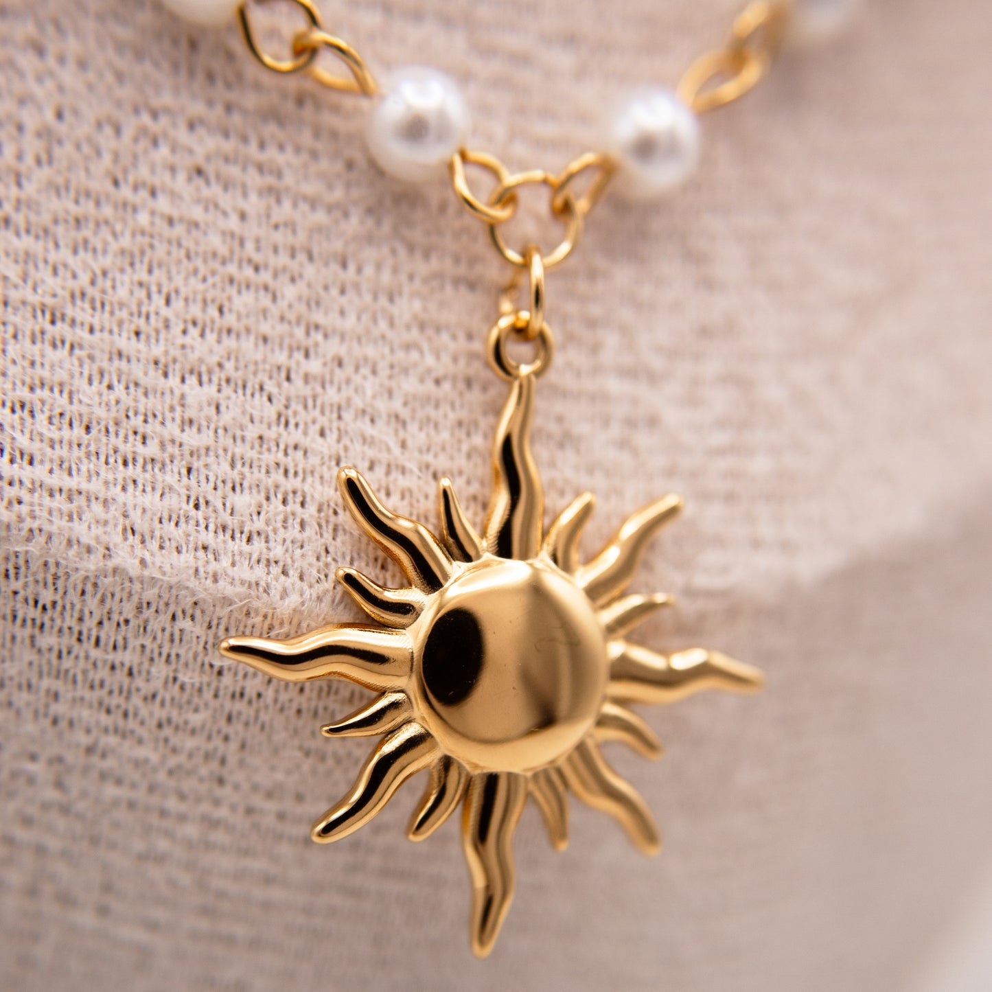 Gold sun-shaped pendant on a chain with pearls against a beige fabric background