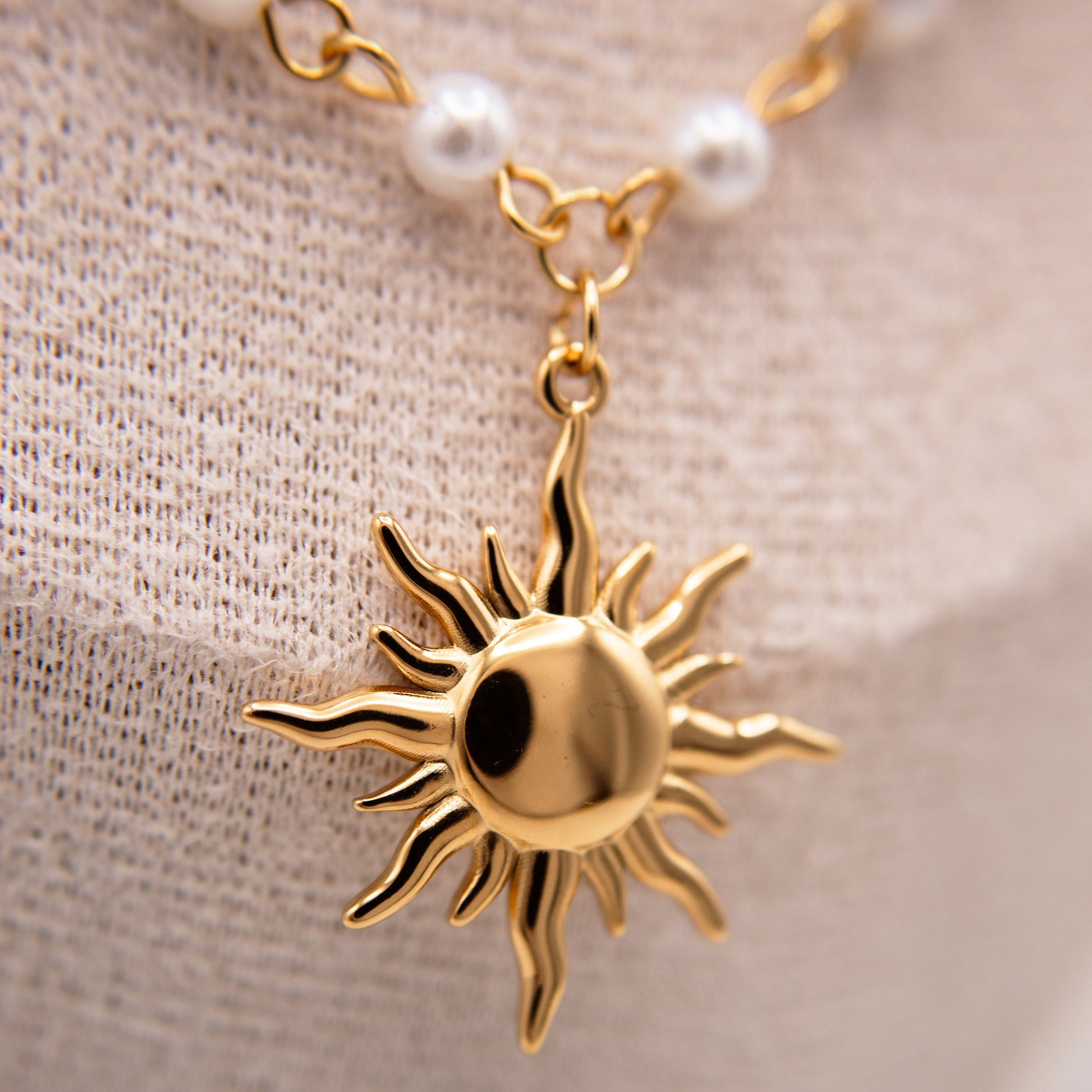 Gold sun-shaped pendant on a chain with pearls against a beige fabric background