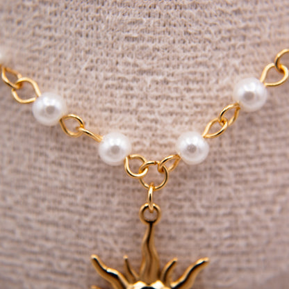 Gold necklace with pearl beads and a sun-shaped pendant on a beige background
