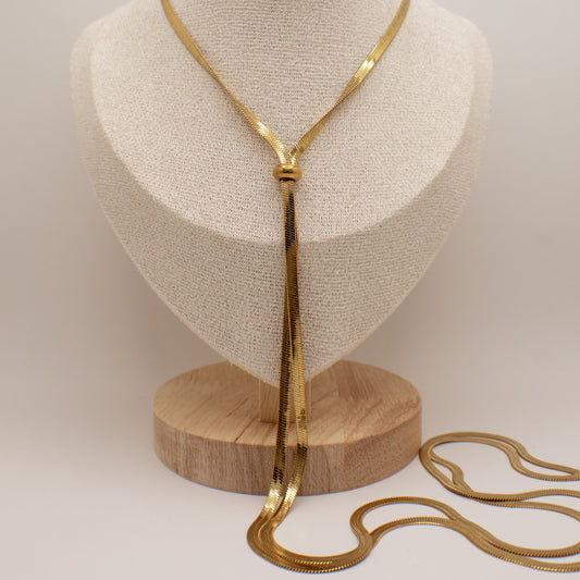 Gold necklace on a wooden stand with a neutral background