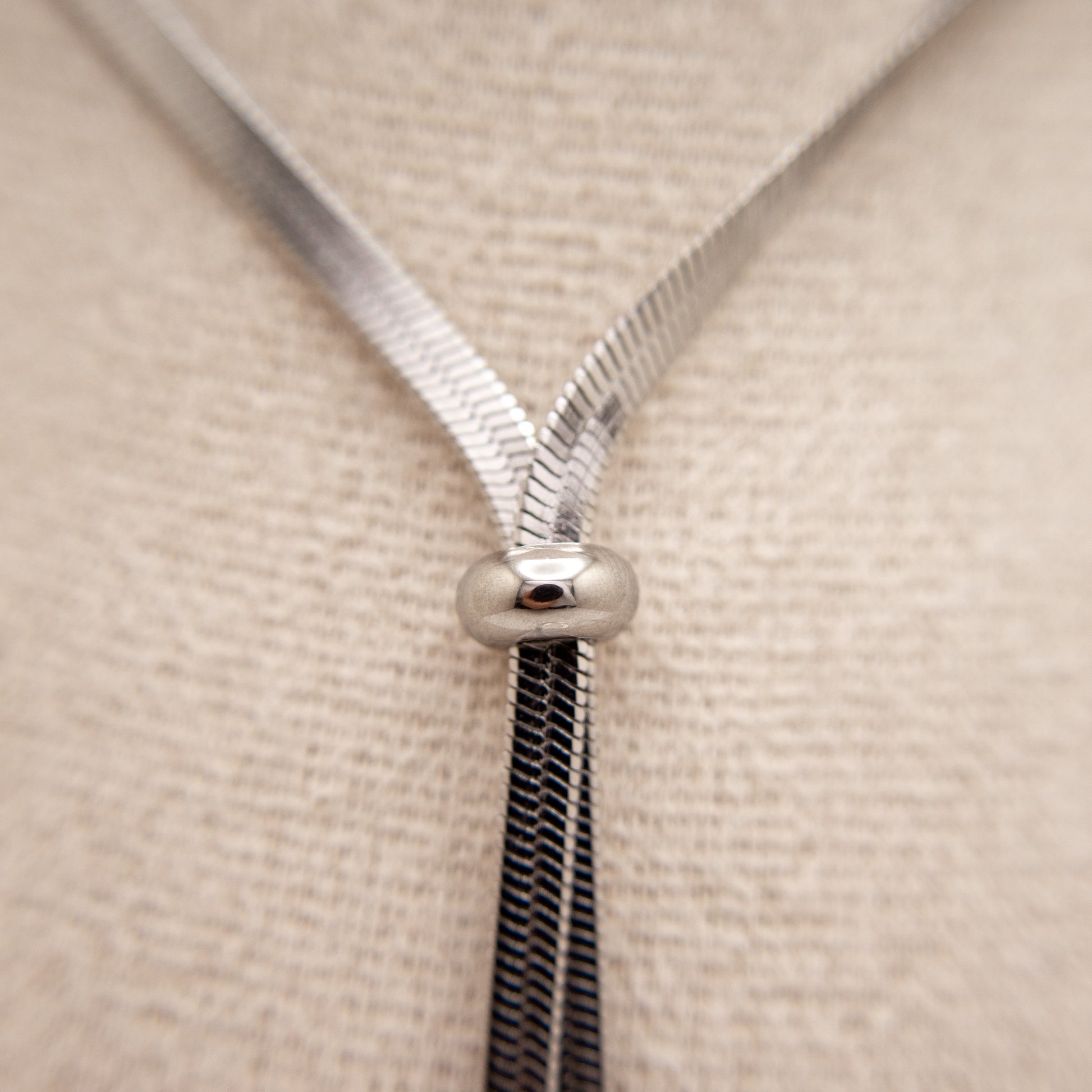 Close-up of a silver necklace with a textured chain on a beige fabric background