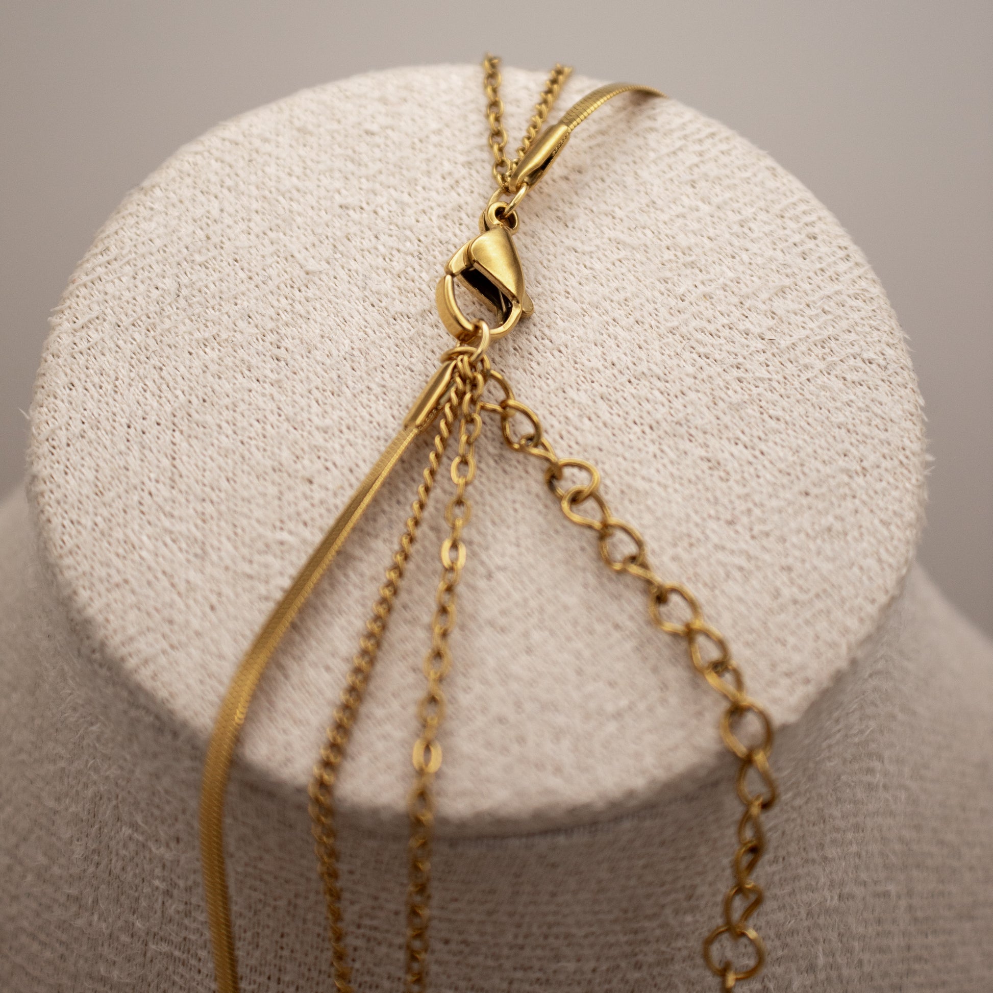 Gold necklace on a white cushioned stand with a neutral background