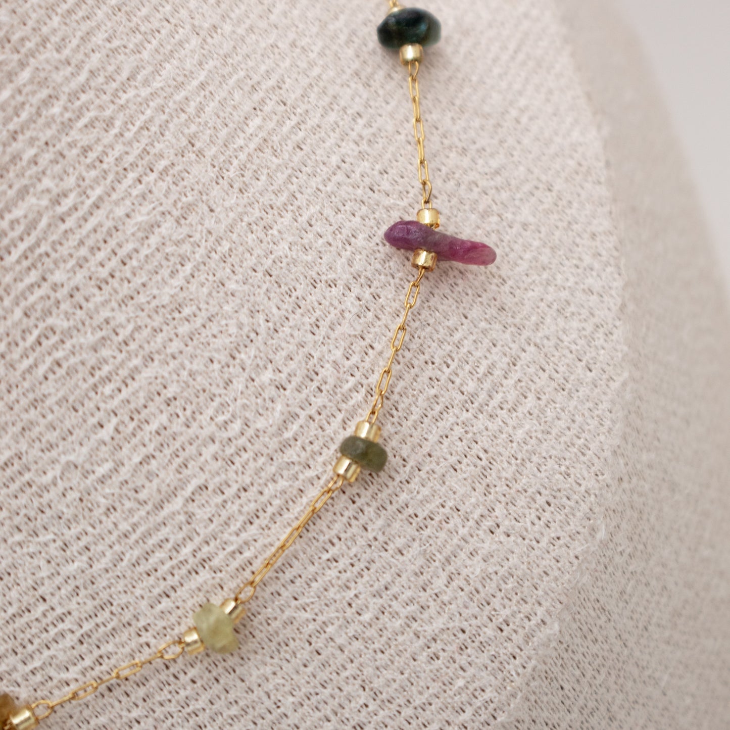 Gold necklace with gemstone beads on a textured beige background