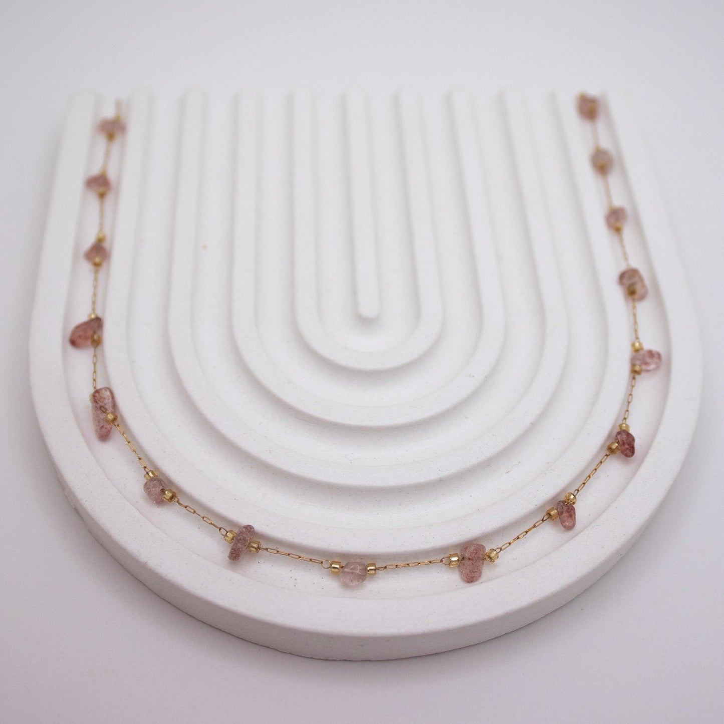 Necklace with pink stones on a white display stand against a light gray background