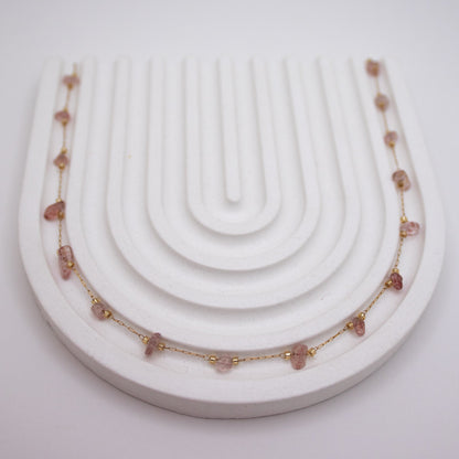 Necklace with pink stones on a white display stand against a light gray background