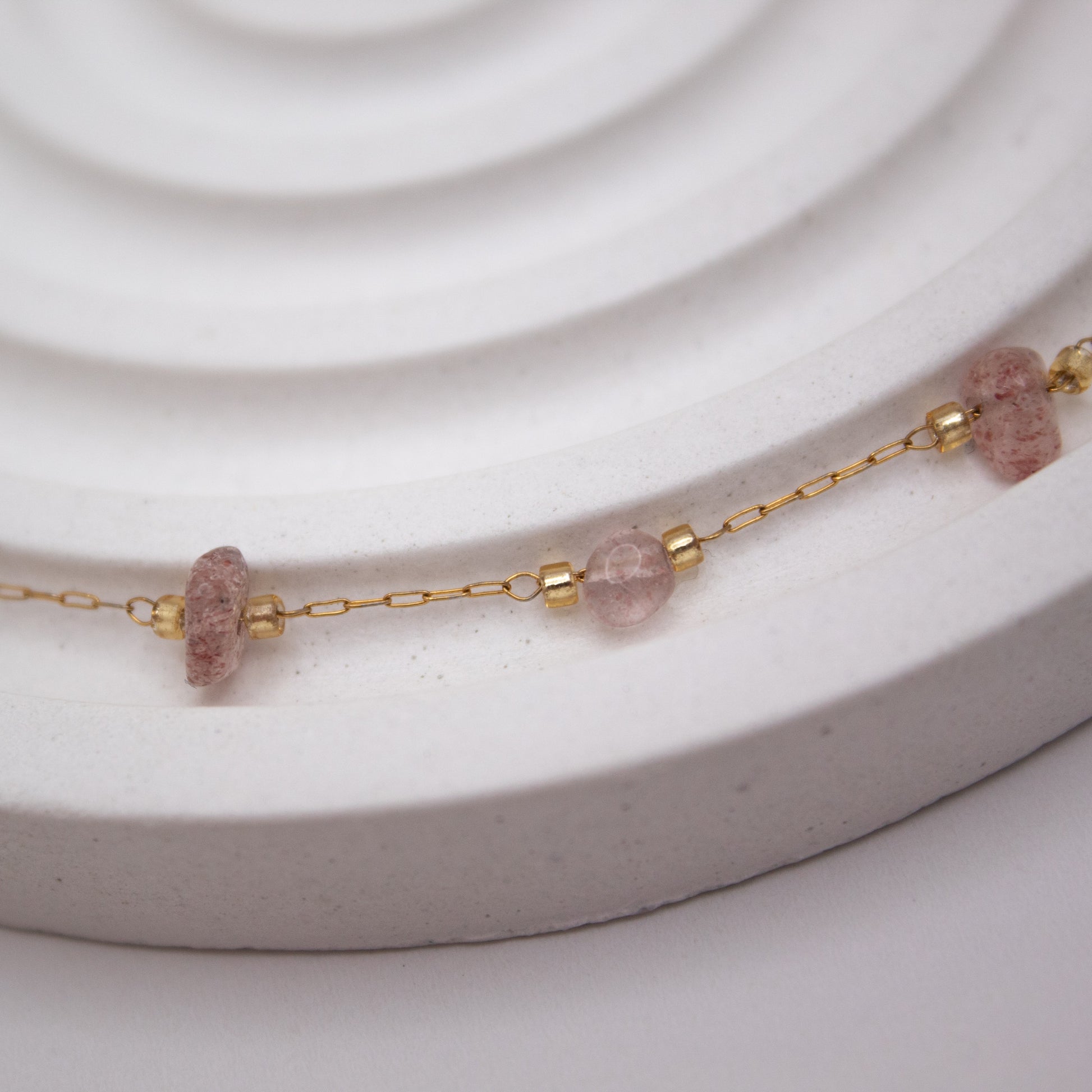 Necklace with pink beads and gold chain on a white surface