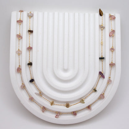 Necklace with pink beads and gold chain on a white surface