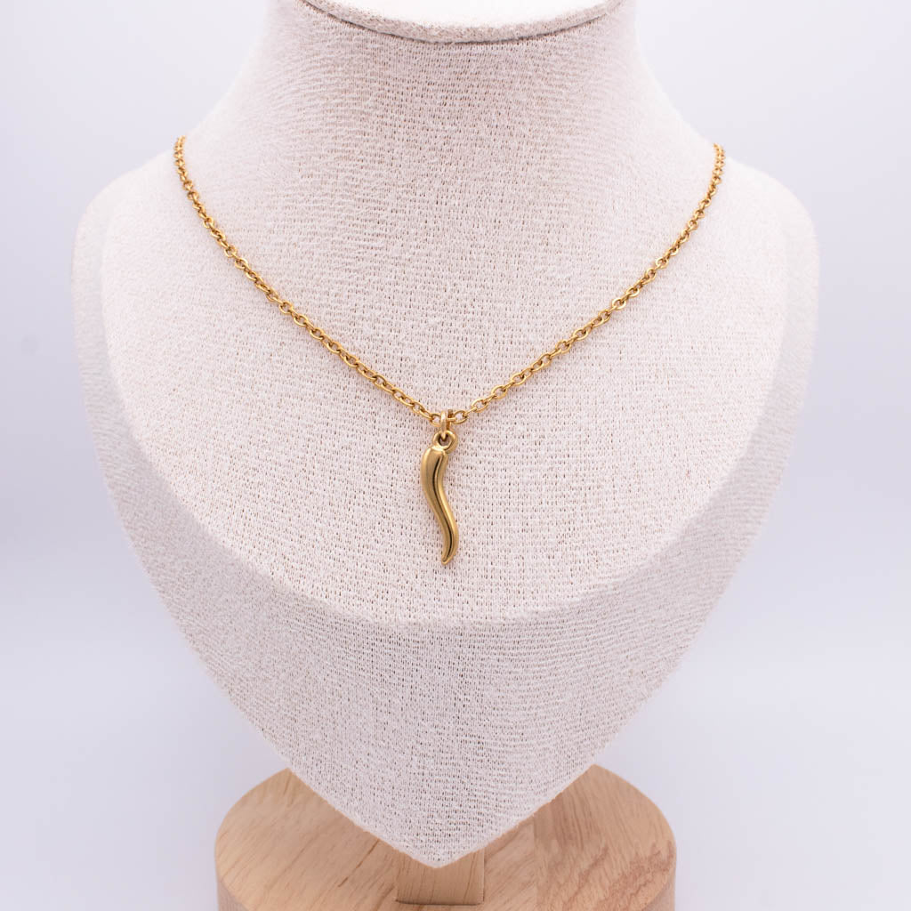 A gold chain necklace with a small curved pendant displayed on a cream fabric jewelry bust against a light gray background.