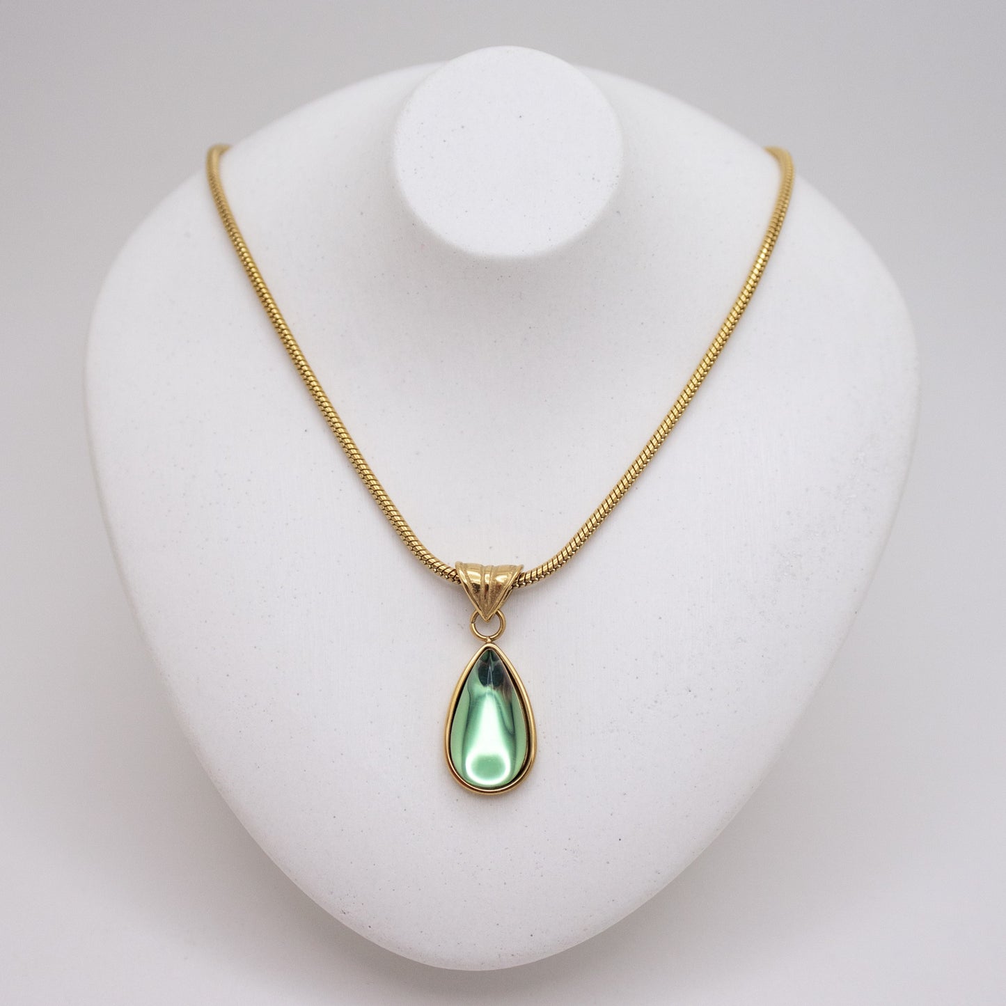 Gold necklace with a green teardrop pendant on a white stand.