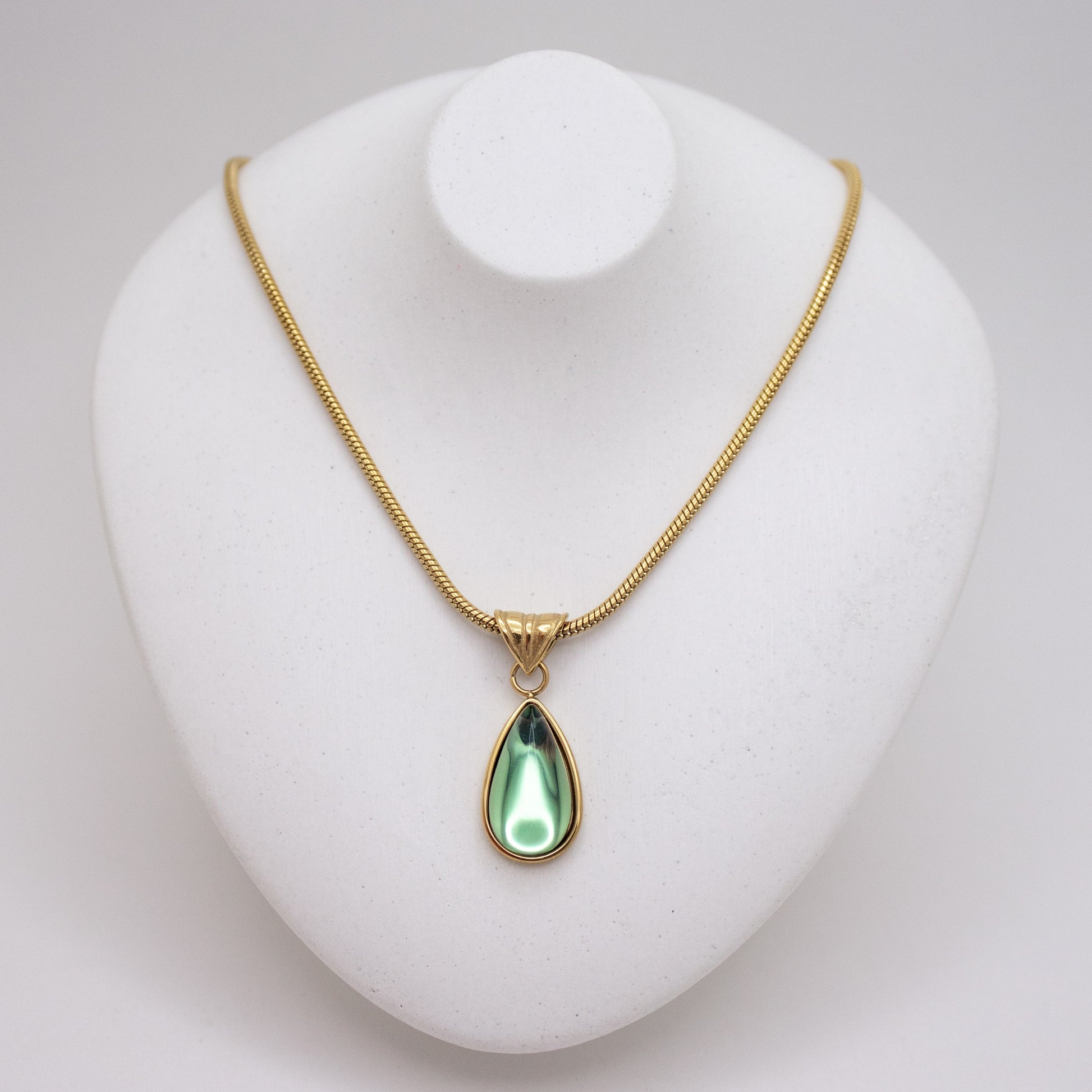 Gold necklace with a green teardrop pendant on a white stand.