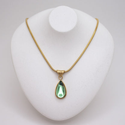 Gold necklace with a green teardrop pendant on a white stand.