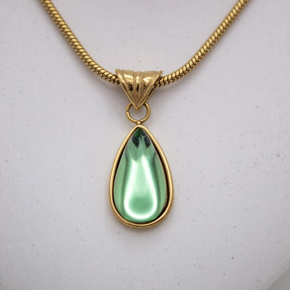 Gold necklace with a green teardrop pendant on a light gray background