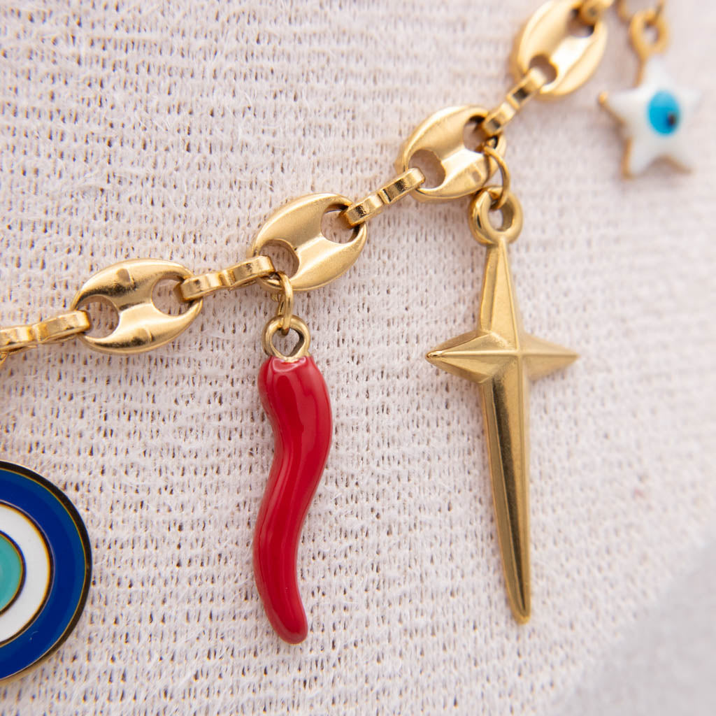 Gold chain bracelet with charms including a red italian horn, a gold star, and partial blue and white evil eye charms, displayed on a textured white fabric.