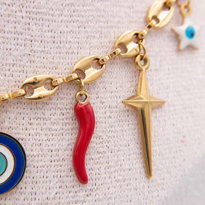Gold chain bracelet with charms including a red italian horn, a gold star, and partial blue and white evil eye charms, displayed on a textured white fabric.