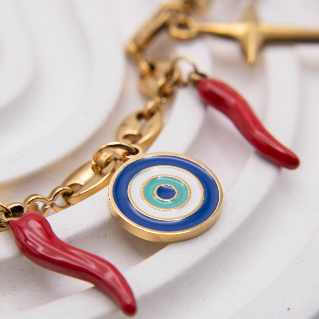 Gold-tone chain bracelet featuring evil eye and italian horn charms on a white textured background.