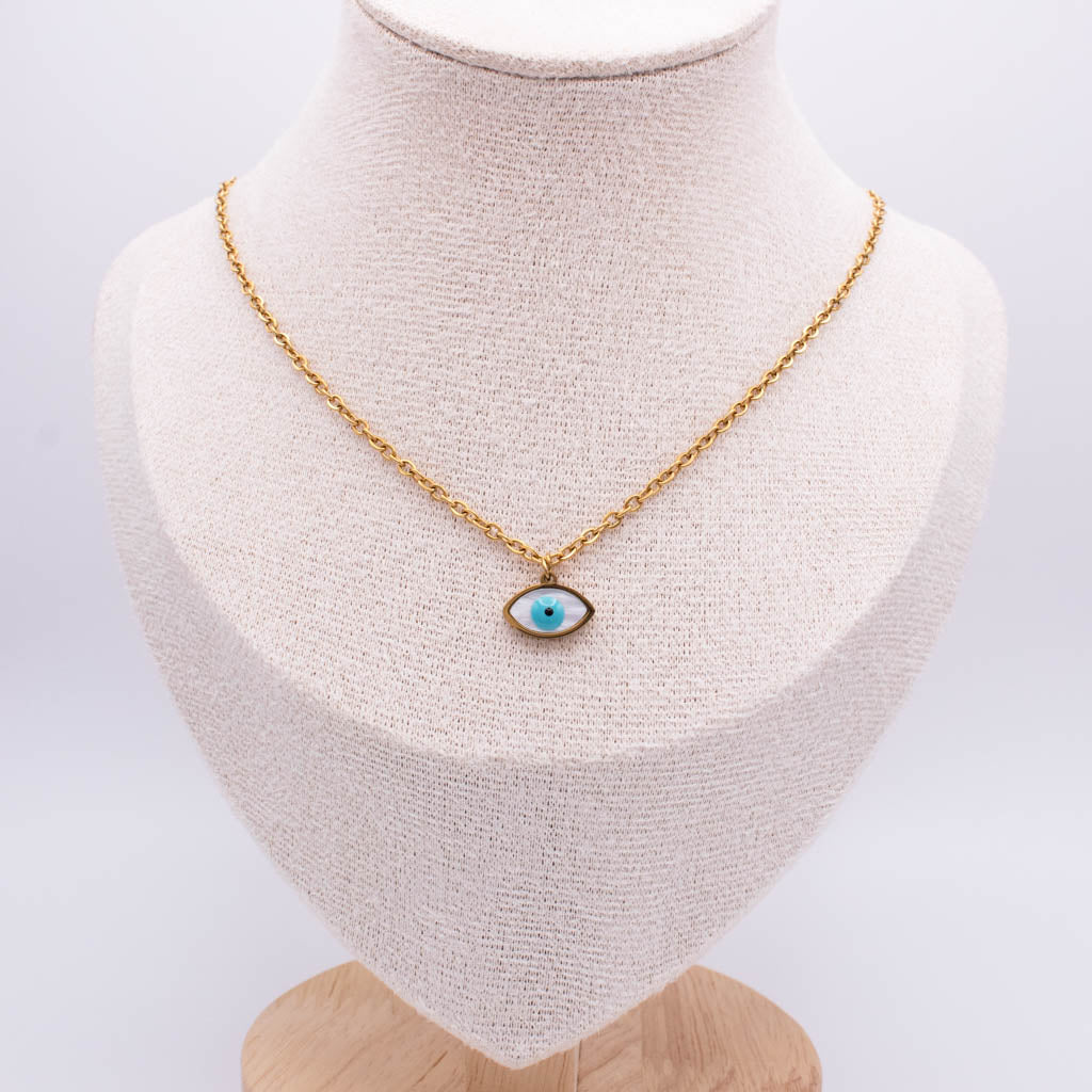 A gold chain necklace with an evil eye pendant displayed on a textured cream fabric jewelry bust against a white background.