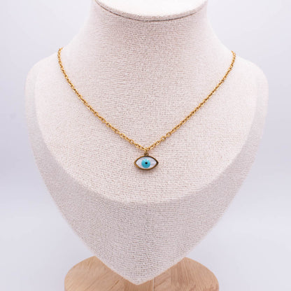 A gold chain necklace with an evil eye pendant displayed on a textured cream fabric jewelry bust against a white background.