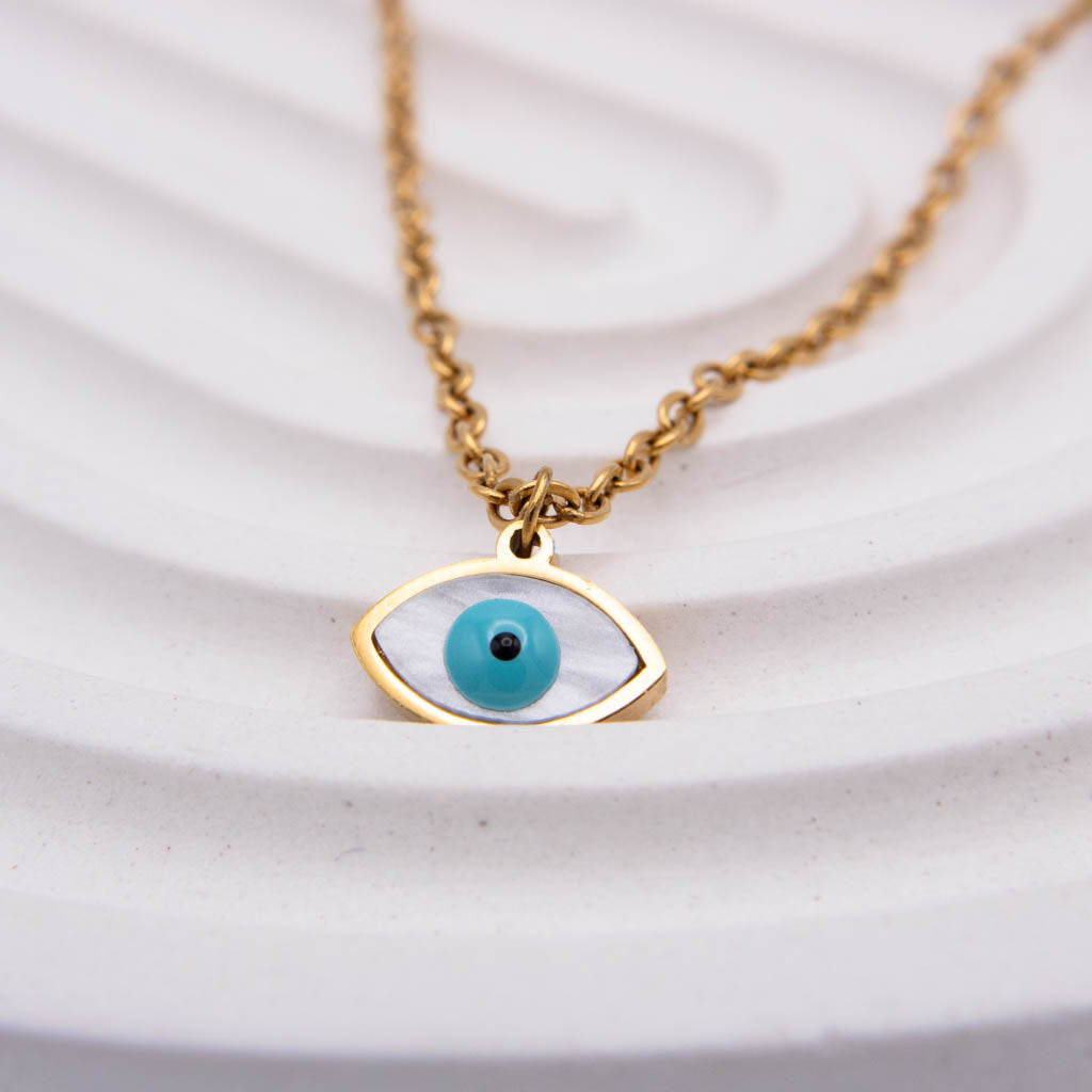 Gold evil eye pendant necklace with a turquoise and black bead center on a white textured background.