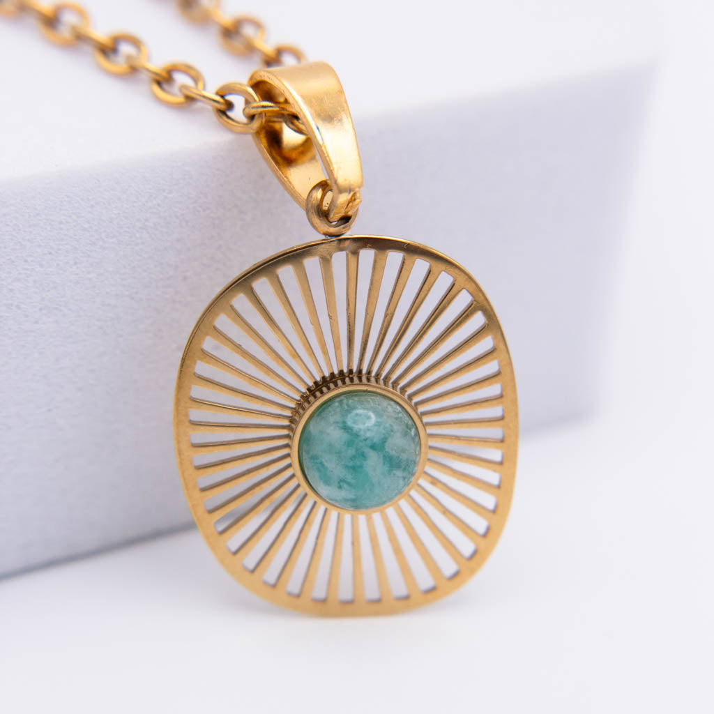 Gold sunburst pendant necklace with a round turquoise-blue stone in the center, shown on a white background.