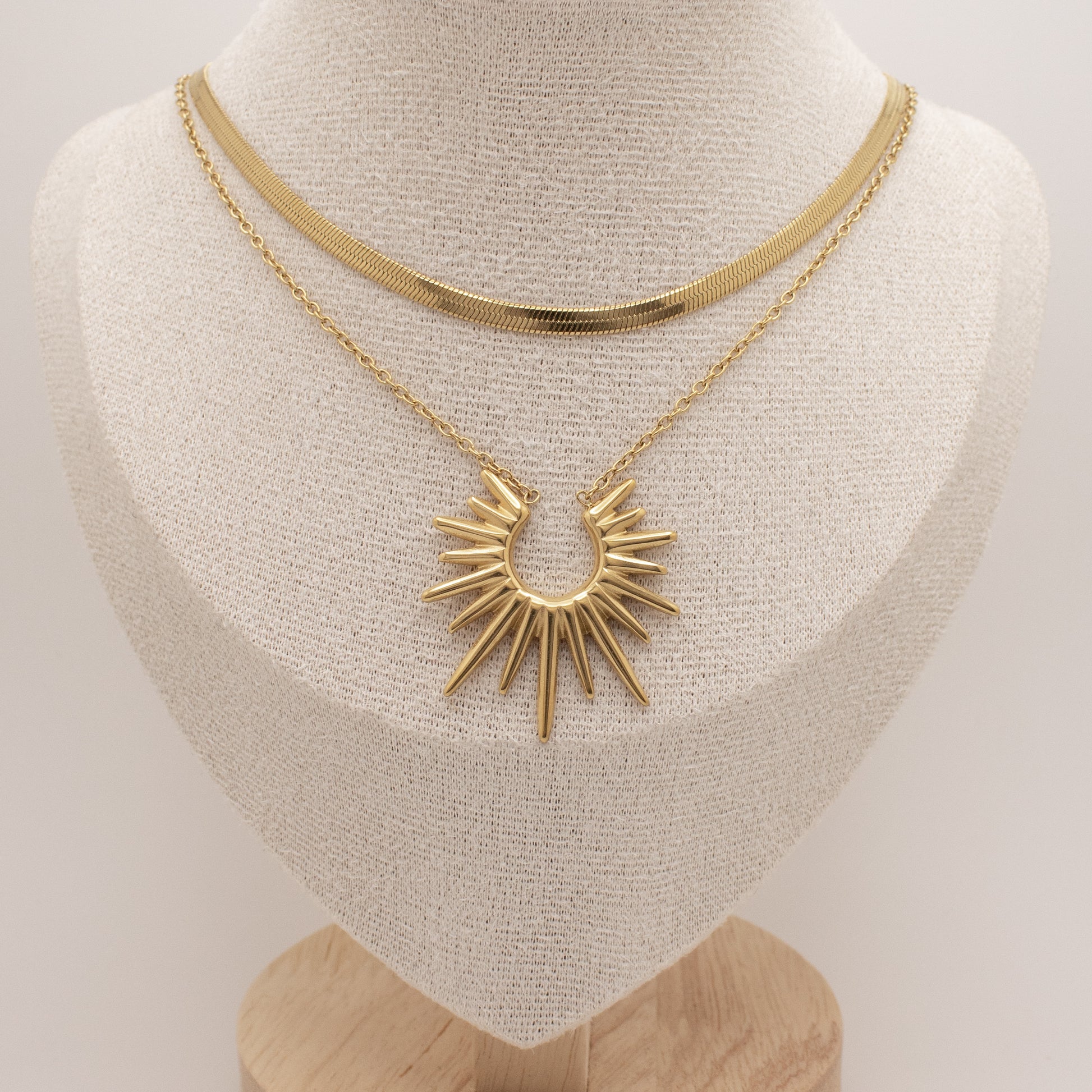 Gold necklace with a sunburst pendant on a mannequin bust.