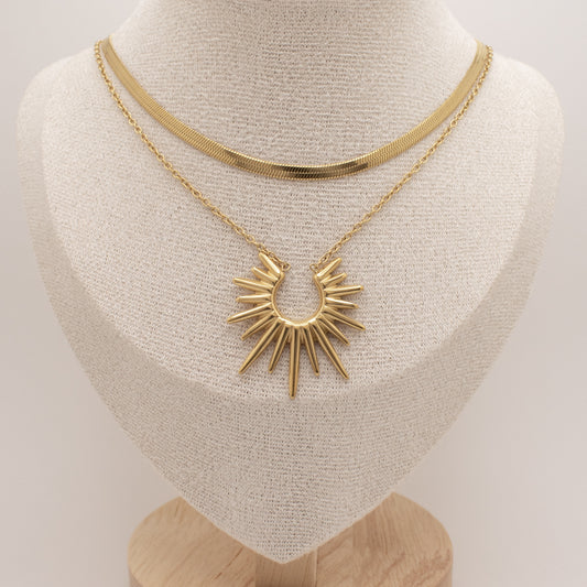 Gold necklace with a sunburst pendant on a mannequin bust.