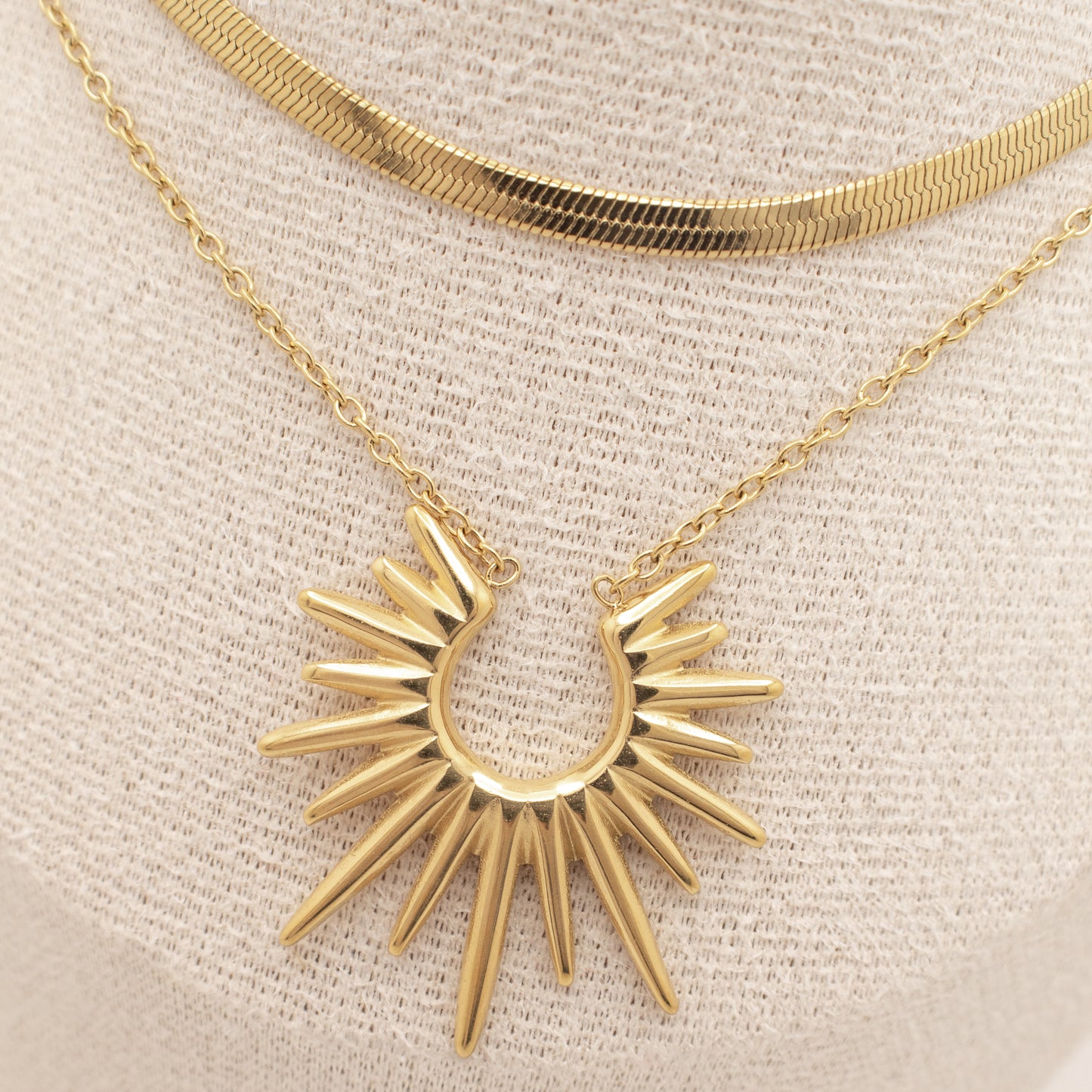 Gold necklace with a sunburst pendant on a beige background