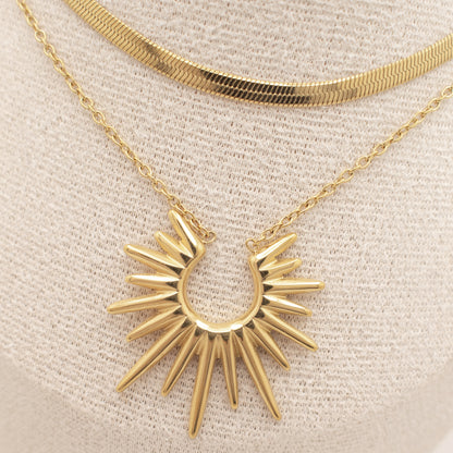Gold necklace with a sunburst pendant on a beige background
