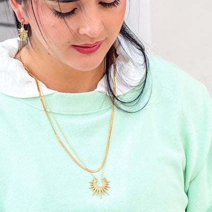Woman wearing a gold necklace with a sun design on a light green background