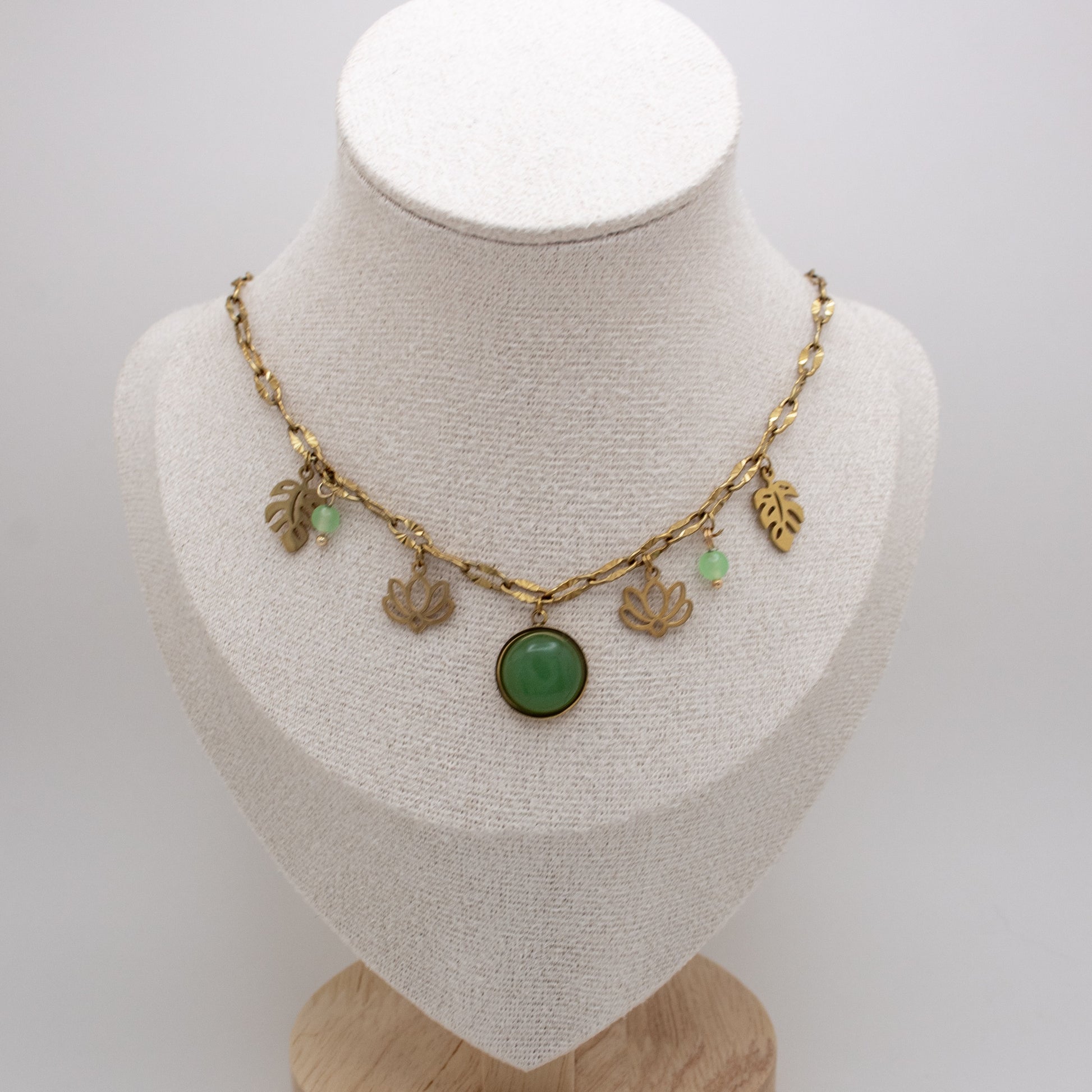 Necklace with green pendant and gold charms on a mannequin bust against a white background
