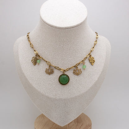 Necklace with green pendant and gold charms on a mannequin bust against a white background