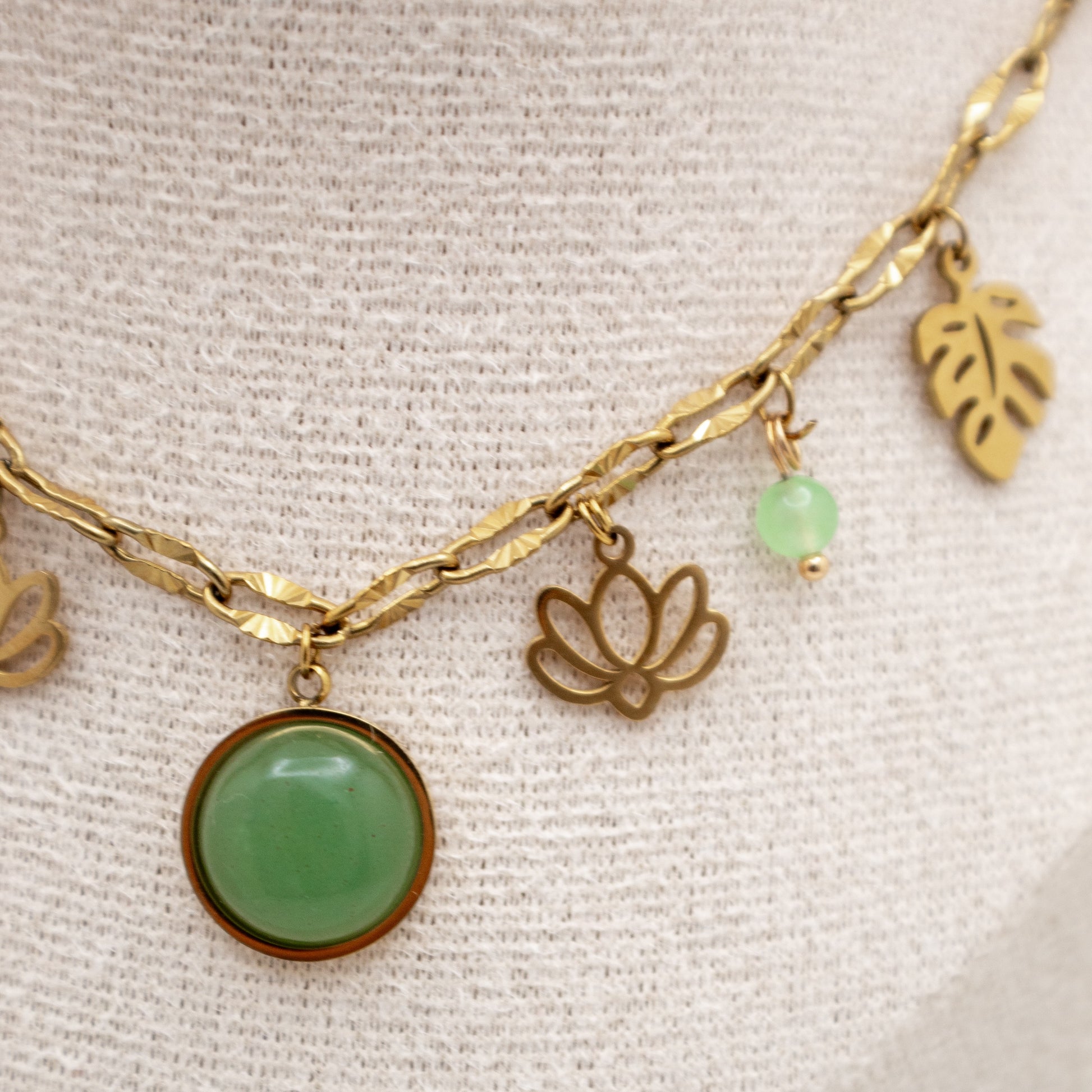Gold necklace with green beads and leaf charms on a textured beige background