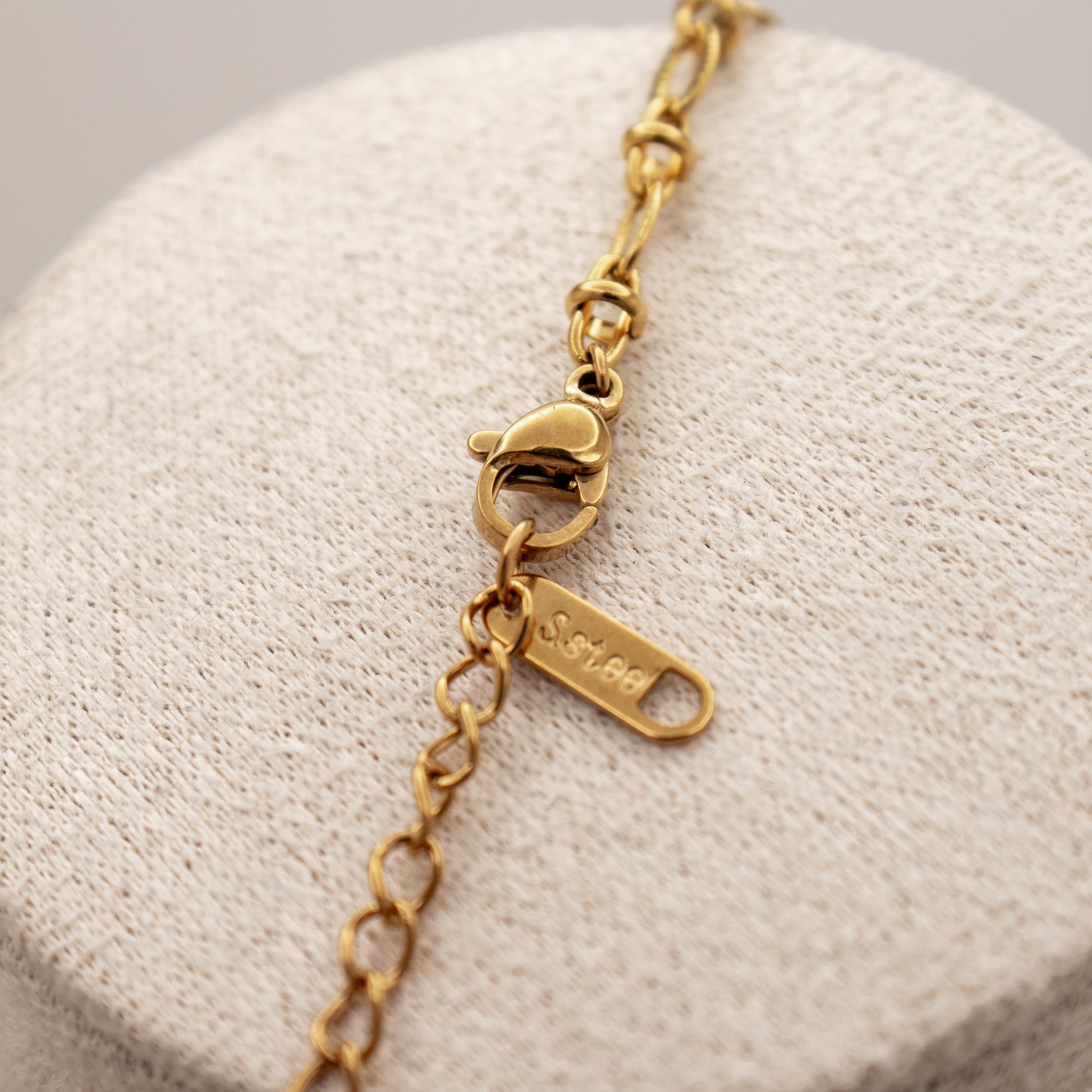 Gold bracelet with a heart clasp on a textured beige surface