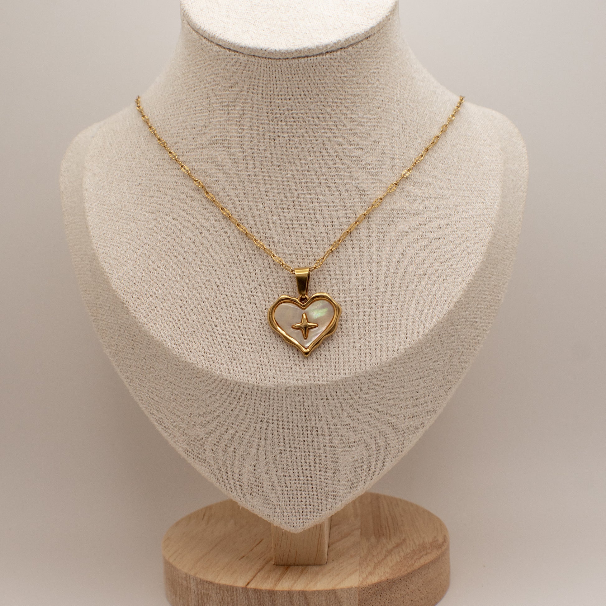 Gold necklace with a heart-shaped pendant on a mannequin bust.