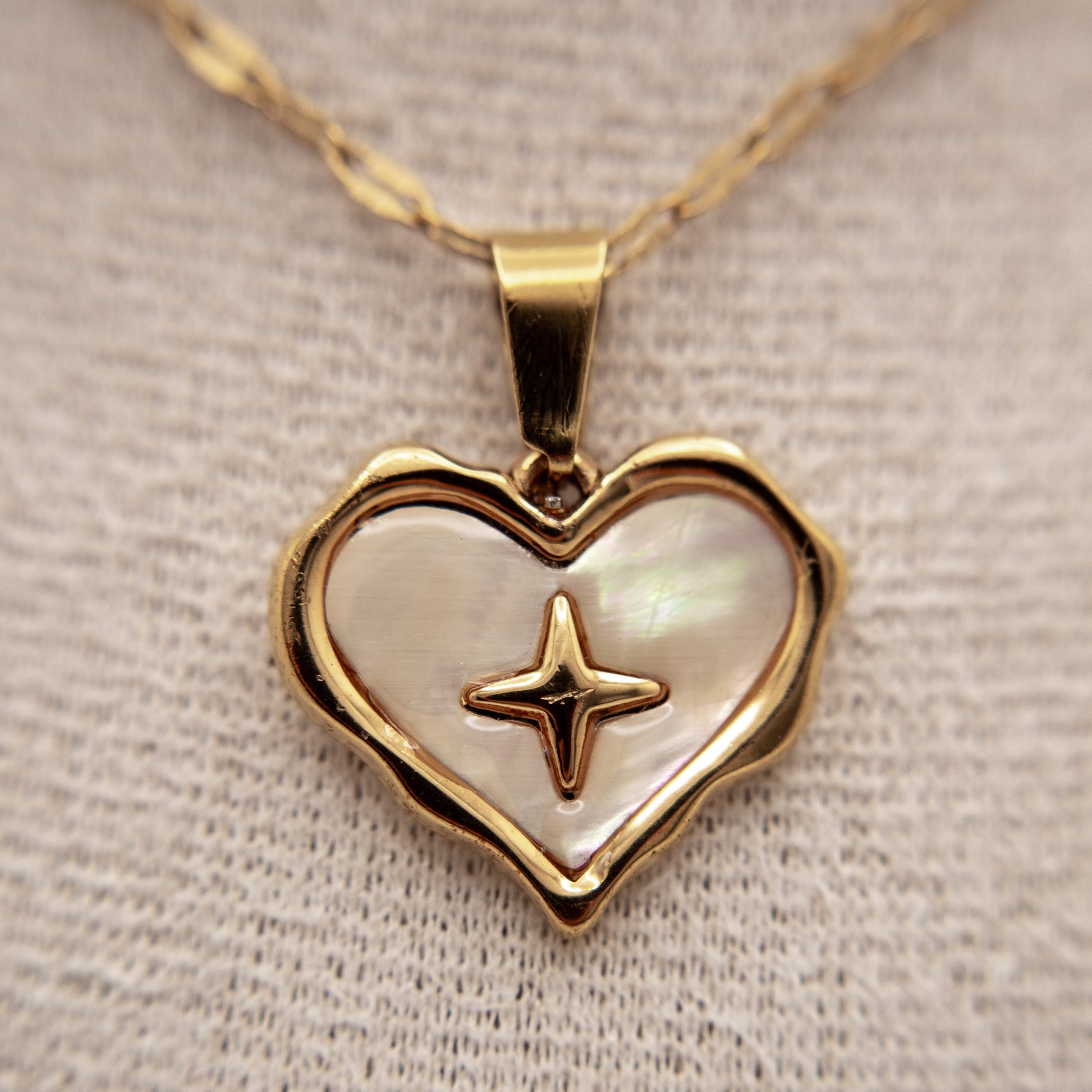 Heart-shaped pendant with star design on a gold chain against a neutral background