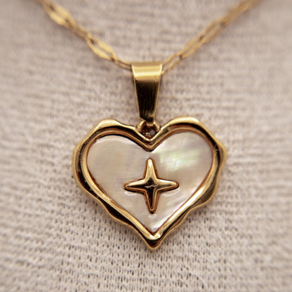 Heart-shaped pendant with star design on a gold chain against a neutral background