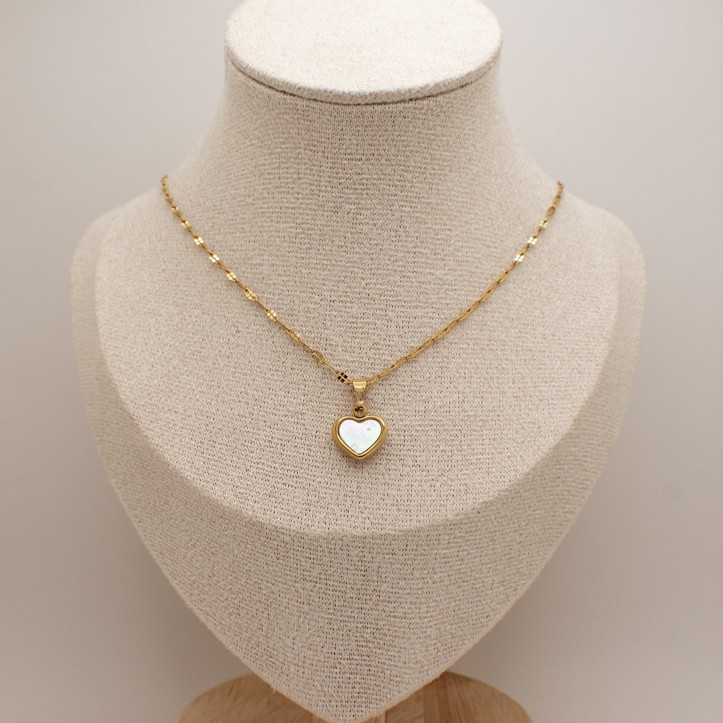 Gold necklace with a heart-shaped pendant on a mannequin bust.
